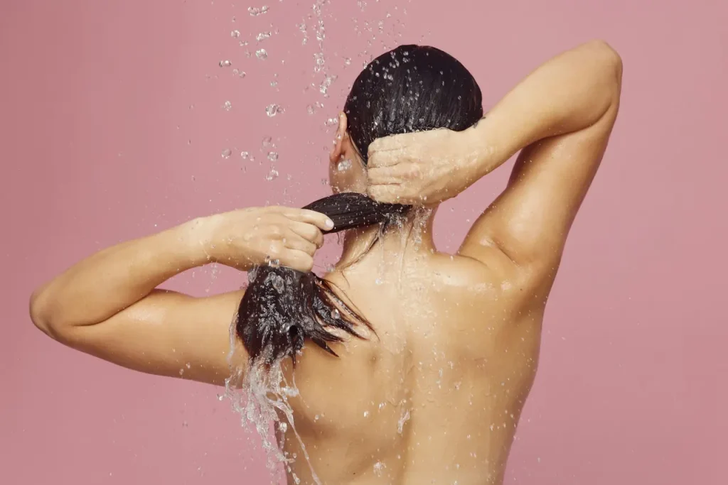 Butelka naturalnego szamponu bez SLS obok zdrowych, błyszczących włosów